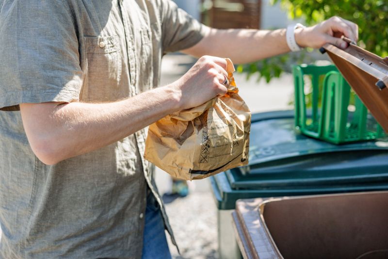 En person slänger en matavfallspåse i ett brunt avfallskärl