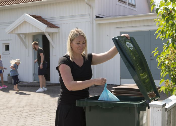 En kvinna slänger en soppåse i sitt gröna kärl för restavfall